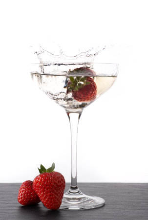 A vertical shot of a strawberry creating a splash when dropped in champagne glassの写真素材