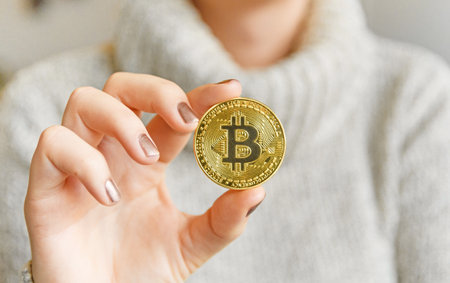A closeup of a woman holding a single bitcoin