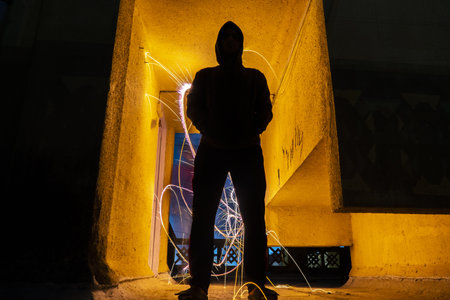 A silhouette of a creepy man standing in a tunnel with light sparklers with long exposure behind him