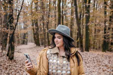 A shot of a woman looking at her phone in an autumn forestの写真素材