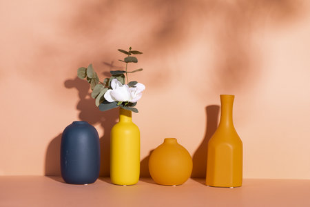 A beautiful white rose in a decorative yellow vase with empty vases against an orange wallの写真素材