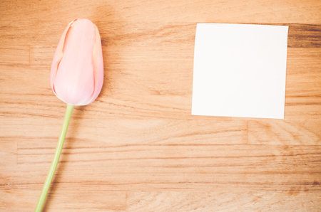 An overhead shot of a pink tulip flower and a blank sticky note on a wooden table with space for your textの写真素材