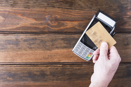 Contactless payment, paypass. Hand hold bank card near terminal on Wooden background copy space.の写真素材