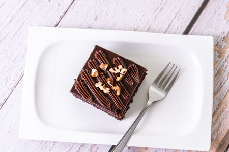 An overhead shot of a slice of chocolate cake topped with nuts on white ceramic plate with a forkの写真素材