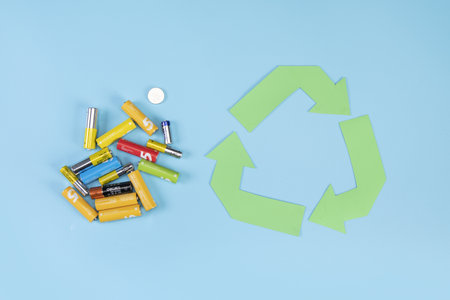 A pile of used batteries on a blue background with a recycling symbolの写真素材
