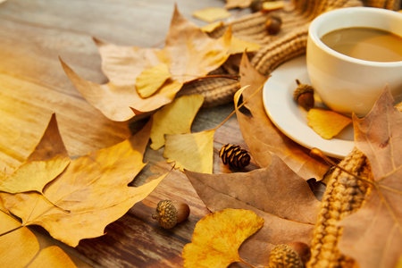 A closeup shot of a cup of coffee and autumn leaves on wooden background