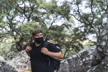 A Caucasian male with a backpack and a medical mask hiking in a forest - the new normal after...