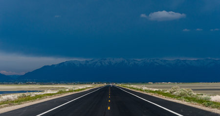 Straight road going towards a very stormy and black sky with the mountains on the horizon under heavy rain.  Angtelope island, Utah, United States ofの写真素材