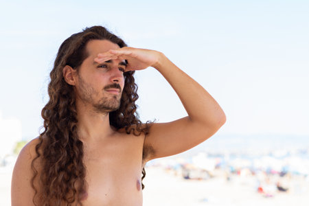 A selective focus shot of an attractive young man with long curly hair on the beachの写真素材