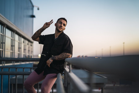 A young stylish tattooed guy sitting on the handrails of a staircase and making the peace gestureの写真素材