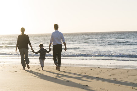 A family of three walking on the seashore during sunsetの写真素材