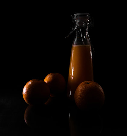 A closeup of oranges and a bottle of fresh juice isolated on a black background under the shadowsの写真素材