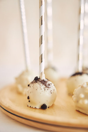 A vertical closeup shot of delicious white Cake pops on a white background and wooden table