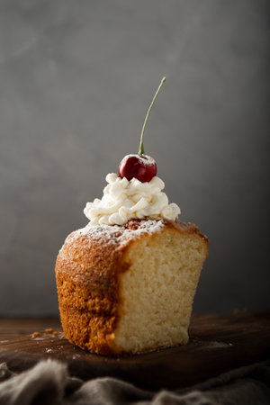 A vertical shot of a delicious cake with cream, powdered sugar, and a cherry on top