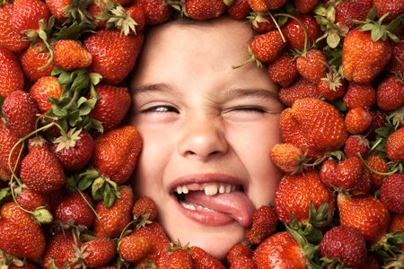 The cute face of a little girl with her tongue out surrounded by strawberriesの写真素材
