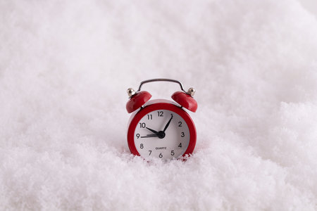 A closeup of a red alarm clock in the snow, a clock counting the time till New Yearの写真素材