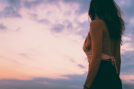 A back view of a sexy female wearing a knitted bikini top and enjoying the sunset at the beachの写真素材