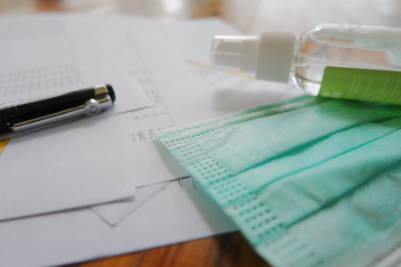 A closeup shot of a facemask, calculator, pen, hand sanitizer, and papers laying on the table