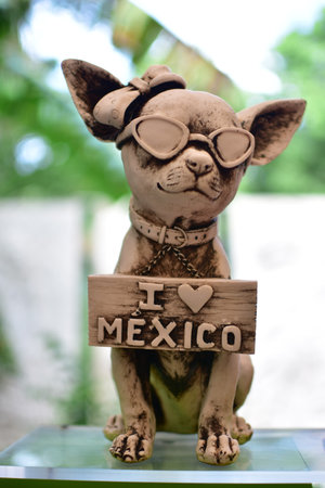 A vertical shot of a cute chihuahua statue with sunglasses and an "I love Mexico" sign in a gardenの写真素材