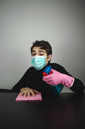 A vertical shot of a young male with a medical mask cleaning and disinfecting a tableの写真素材