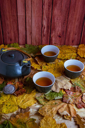 A vertical shot of gray tea set on autumn leaves and wooden background