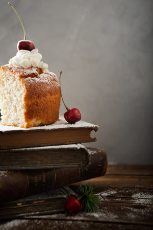 A vertical shot of a delicious cake with cream, powdered sugar, and cherries on booksの写真素材