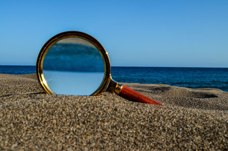 A closeup shot of a loupe magnifying glass on a sandy beachの写真素材