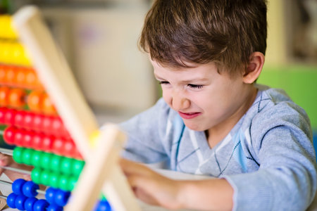A cute Caucasian baby boy feeling bored and frustrated while playing with an abacus at kindergarten