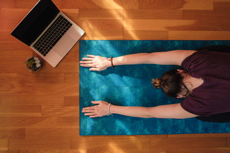 A female stretching over a mat during online yoga classの写真素材