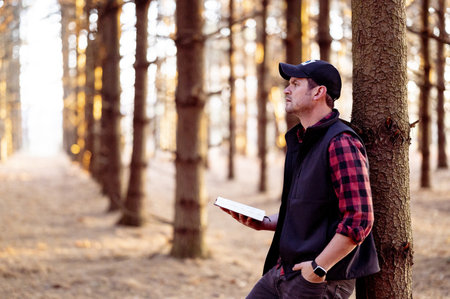 A selective focus shot of a man holding a book posing in a forestの写真素材