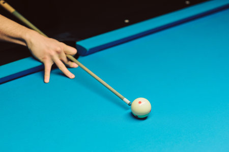 A hand with cue stick pointing at a ball on billiard table