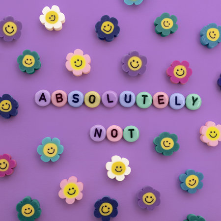 Some plastic beads with letters form the words "ABSOLUTELY NOT" and there are some smiley flower beads around it. Background is purple.の写真素材