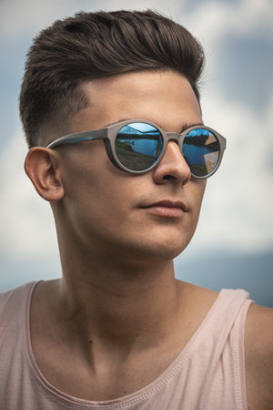A closeup vertical portrait of a stunning young male wearing trendy sunglasses with nature...