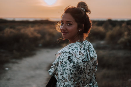 A shallow focus of a stylish young female with her hair in a messy bun in a field during the sunsetの写真素材