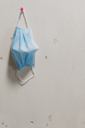 A vertical shot of a used disposable mask hanging on a white wall - precaution, disease control...