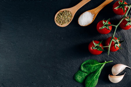 An overhead shot of cherry tomatoes, garlic, and wooden spoons full of spice on a dark backgroundの写真素材