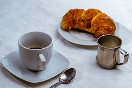 A closeup shot of a cup of coffee and croissant on the table