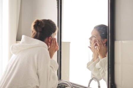 A young female looking in the mirror and touching her face skinの写真素材