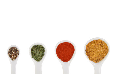 An overhead shot of a collection of spices on spoons isolated on white background