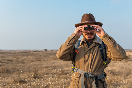 A Caucasian hiker man with a beard, wearing a brown jacket, backpack, looking through binocularsの写真素材