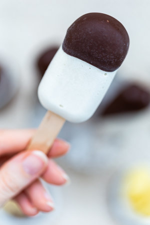 A vertical closeup shot of a female hand holding a raw vegan ice-cream on stickの写真素材