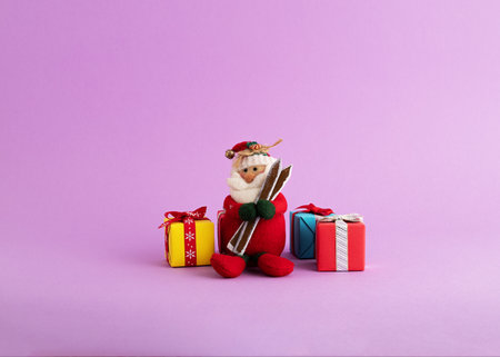 A closeup of a cute Santa Claus toy and colorful gift boxes in the purple backgroundの写真素材