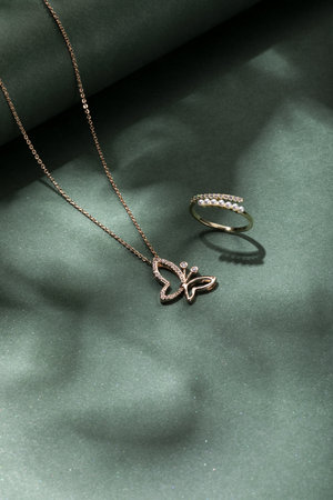 A top view vertical closeup of a gold necklace and a pearl ring on a green backgroundの写真素材