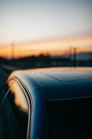 A closeup shot of raindrops on a car top with the sunset sky reflecting in the windowsの写真素材