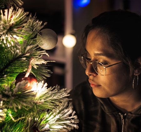 A closeup of a Hispanic female with eyeglasses looking at an illuminated Christmas treeの写真素材
