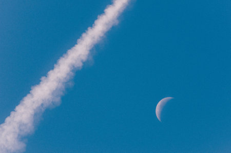 Beautiful shot of contrail and the moon during daytimeの写真素材