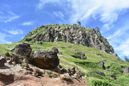 A closeup shot of a rocky hill with green grass and blue sky on the backgroundの写真素材