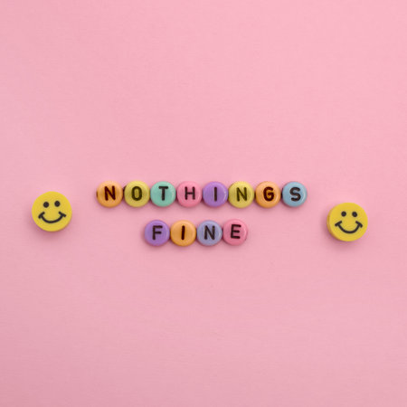 Some plastic beads with letters form the words "NOTHING'S FINE" and there are two yellow smiley beads around it. Background is pink.の写真素材