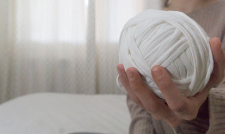 A closeup of a hand holding a white t-shirt yarn ball on a blurry backgroundの写真素材