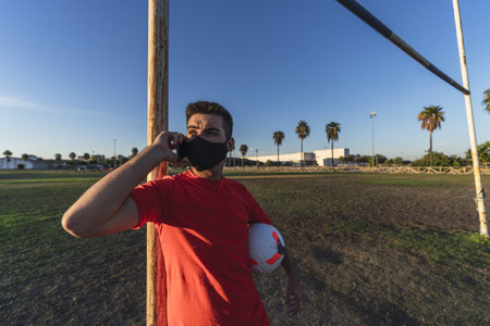 A soccer player in a mask holding a ball and talking on the phone, the concept of a healthy...